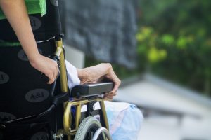 Close-up of a caregiver pushing an elderly person in a wheelchair outdoors