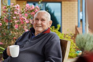 Male Home Care Package client sitting outside with a cup and smiling