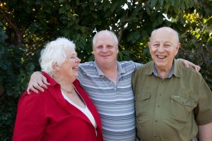 Male NDIS client smiling with his arms over his parents' shoulders