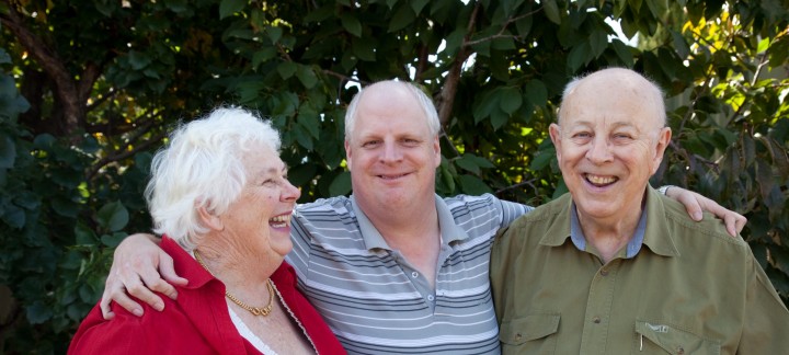Male NDIS client smiling with his arms over his parents' shoulders