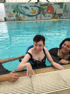 Woman swimming with help from her female disability care workers