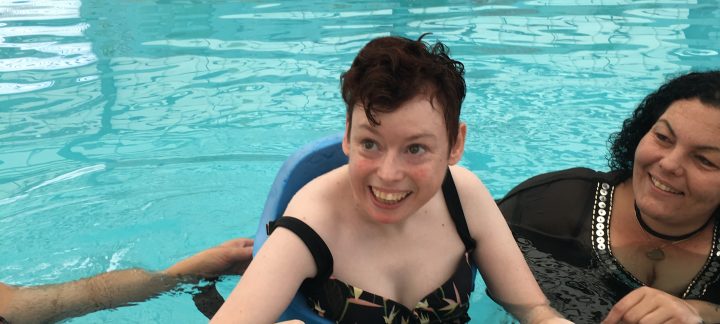 Woman swimming with help from her female disability care workers