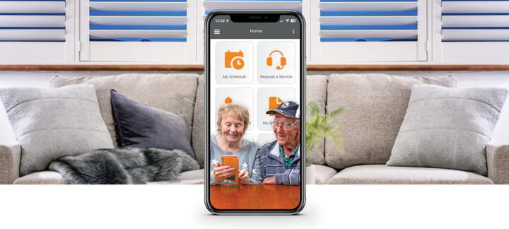Home screen of the Mercy Health Healthy Ageing app on an iPhone with a client's lounge in the background